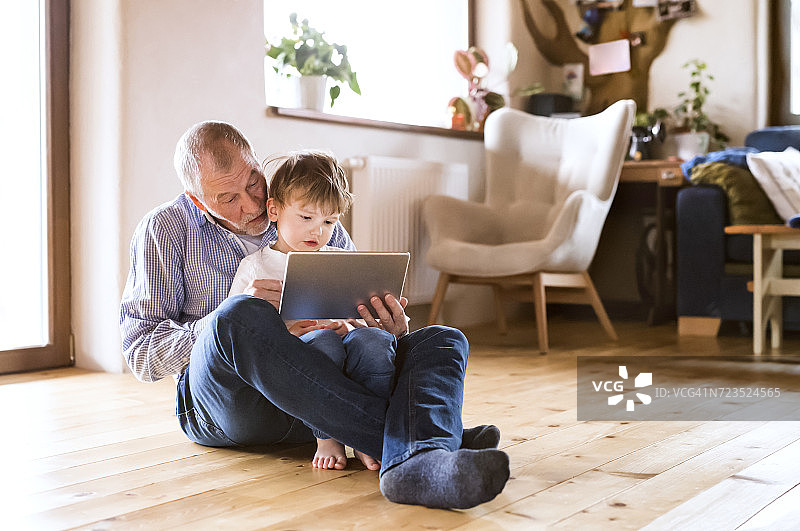 爷爷和孙子坐在地板上，用着数字平板电脑图片素材