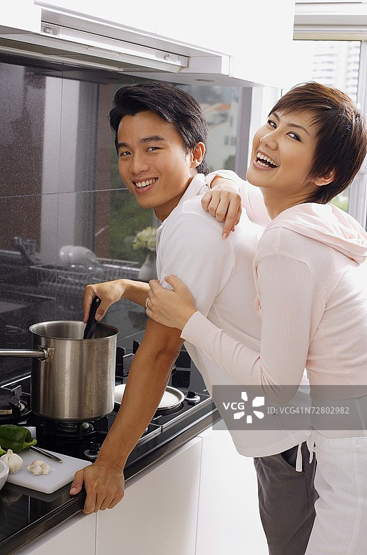 男人在炉子上做饭，女人从后面拥抱他，两人都看着镜头图片素材