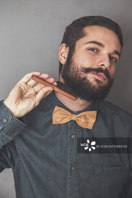 一名男子穿着牛仔衬衫，打着软木领结，用木刷梳理着胡子图片素材