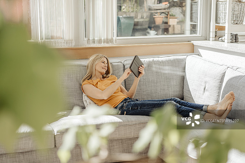 女人坐在家里的沙发上，喝着咖啡，吃着平板电脑图片素材
