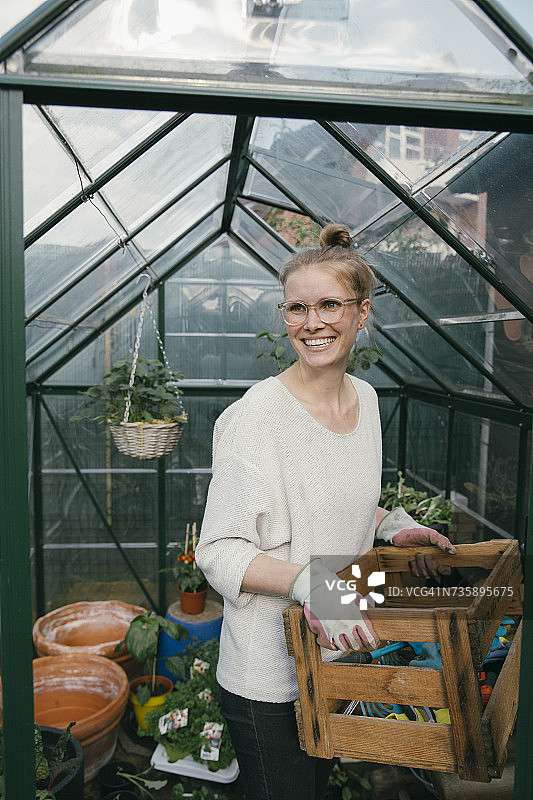 微笑的年轻女子的肖像与园艺工具在温室前的盒子图片素材