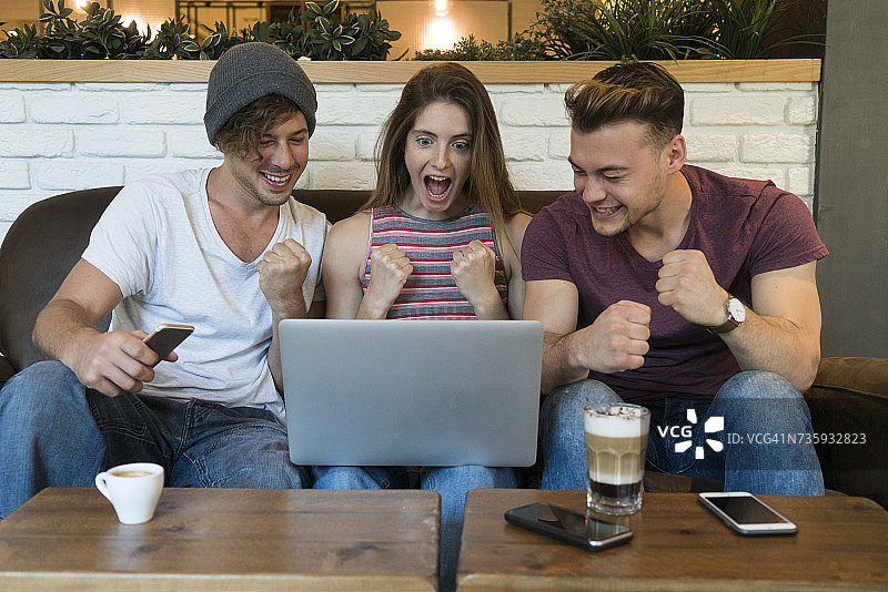 三个兴奋的朋友在咖啡馆看笔记本电脑图片素材