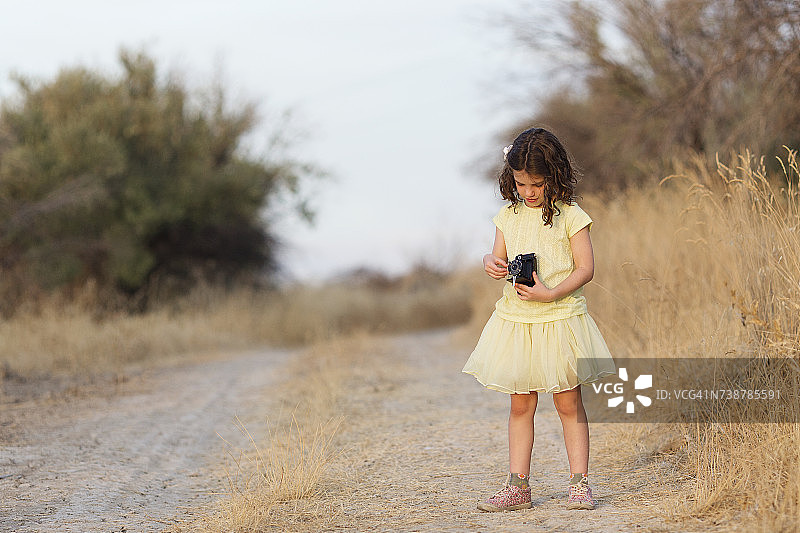 西班牙安达卢西亚，一个女孩拿着一台老式相机站在乡间小路上图片素材