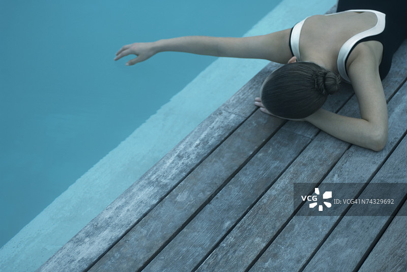 穿着泳衣的女子躺在泳池旁的甲板上，用手触摸水面图片素材