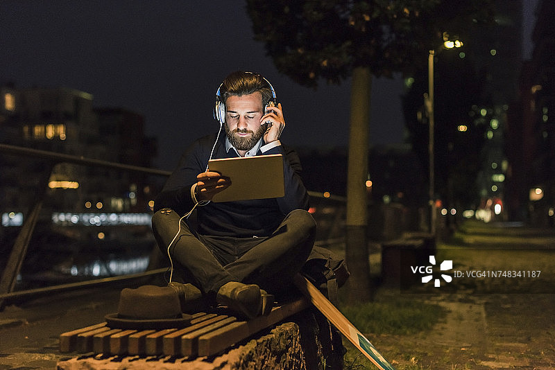 年轻人晚上带着平板电脑和耳机在城市里图片素材