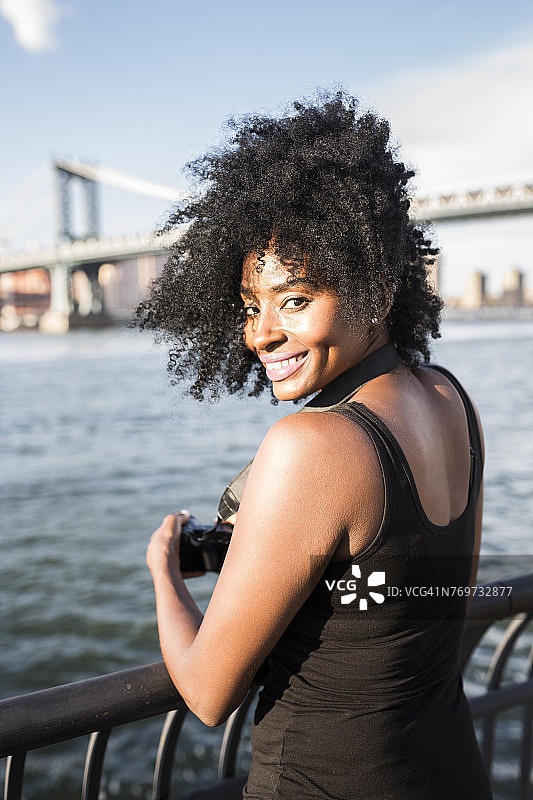 美国，纽约市，布鲁克林，微笑的女人站在水边的肖像图片素材