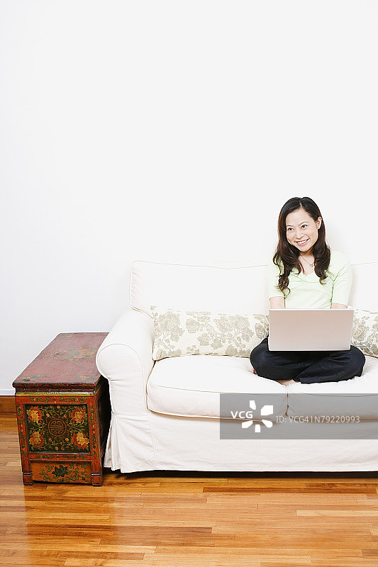 一个坐在沙发上用笔记本电脑的年轻女人图片素材