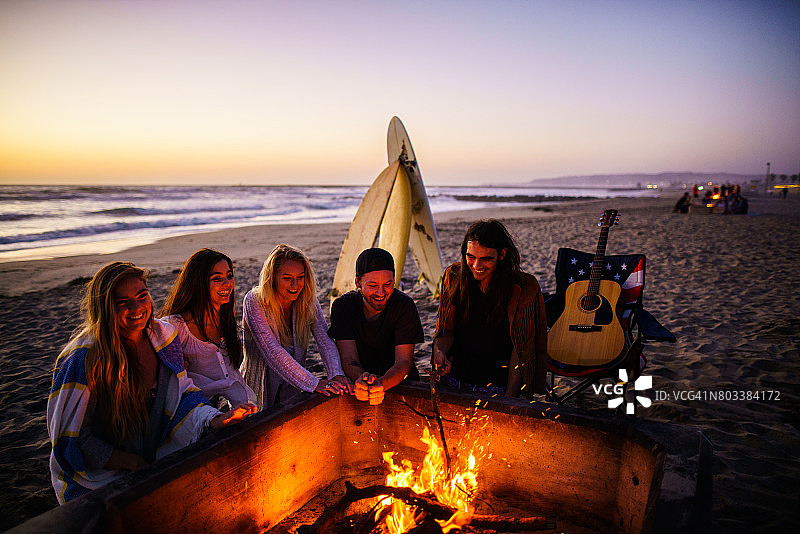 多民族的年轻人，花时间在圣地亚哥的海滩上看日落，弹吉他，在火旁取暖图片素材