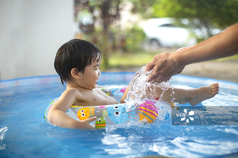 亚洲蹒跚学步的男孩漂浮在水上充气游泳池。图片素材