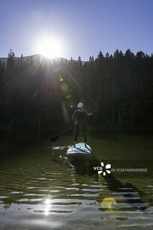 女人站起来划桨板在美丽的山湖图片素材