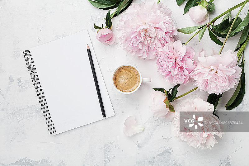 早餐用的咖啡杯，空笔记本，铅笔和粉红色的牡丹花。平的。女人工作的办公桌。图片素材