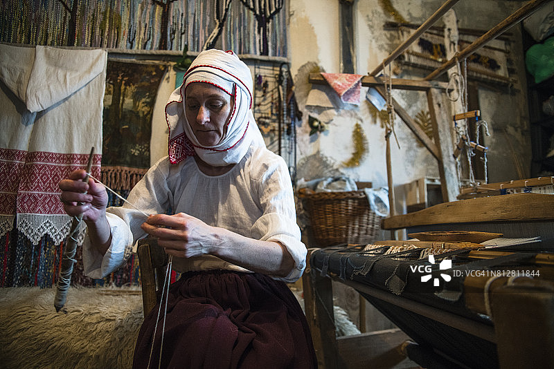 成熟的白俄罗斯妇女穿着传统服装在老式织布机旁纺纱图片素材