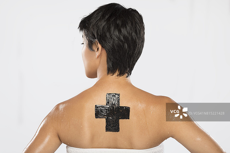 一位棕褐色的女士展示了一个十字架开裂的木炭面具，被放在她的背上图片素材