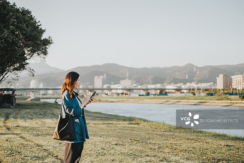日落时分，一位年轻女士在河边的公园里用智能手机图片素材