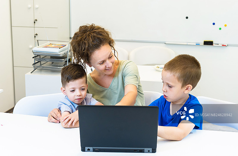 女老师在教室里学用笔记本电脑的两个学龄前男孩图片素材