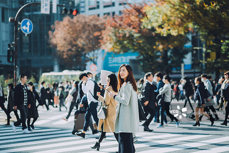 美丽的亚洲女商人在东京繁华的街道上使用智能手机图片素材