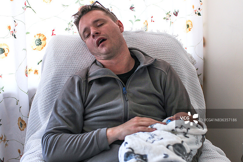 一位父亲抱着医院里刚出生的男婴睡着了。图片素材