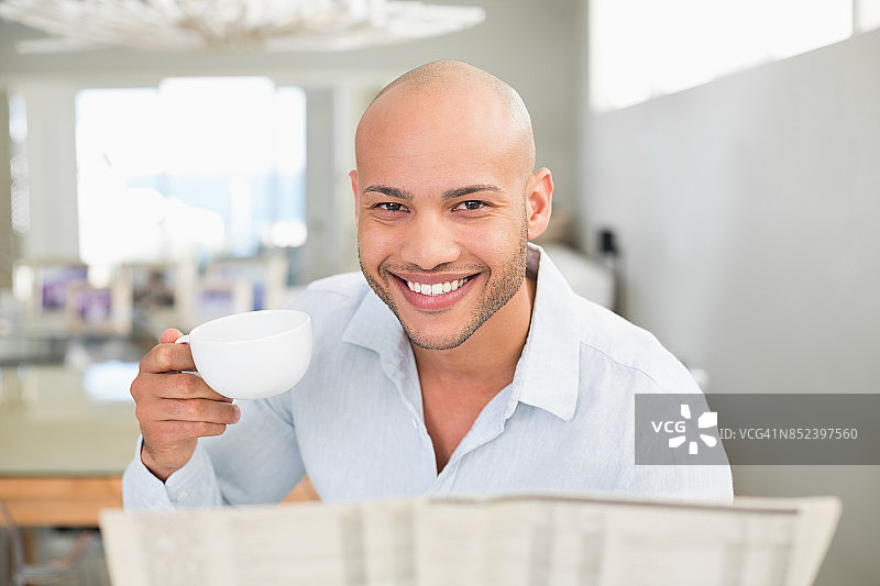 微笑的男人拿着咖啡杯在家看报纸图片素材