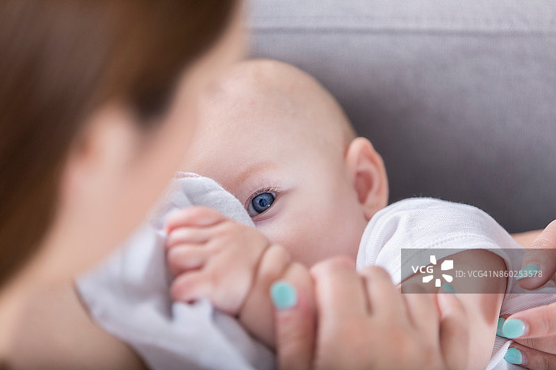 可爱的蓝眼睛婴儿看着妈妈在母乳喂养图片素材