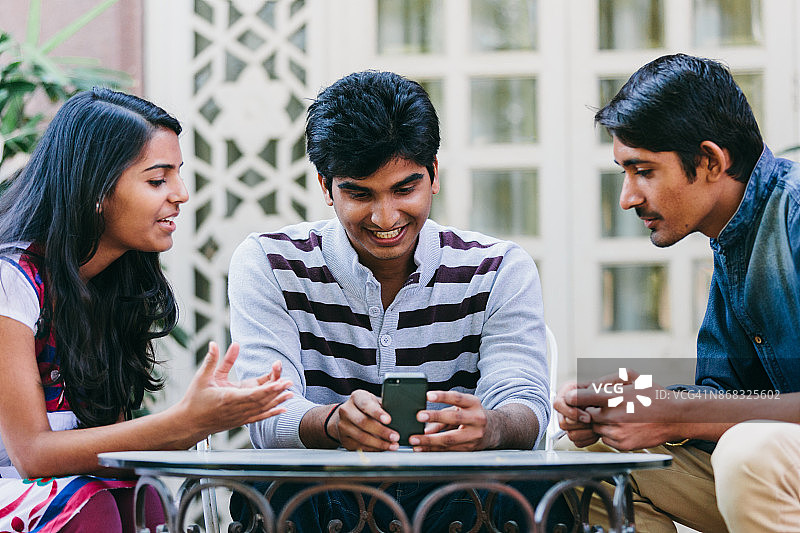 一群印度千禧一代围坐在院子里的桌子旁看智能手机。图片素材