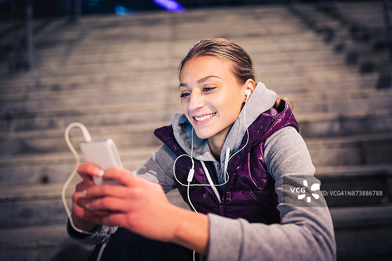 女性在运动。年轻女子在运动训练后休息，听音乐，玩智能手机图片素材