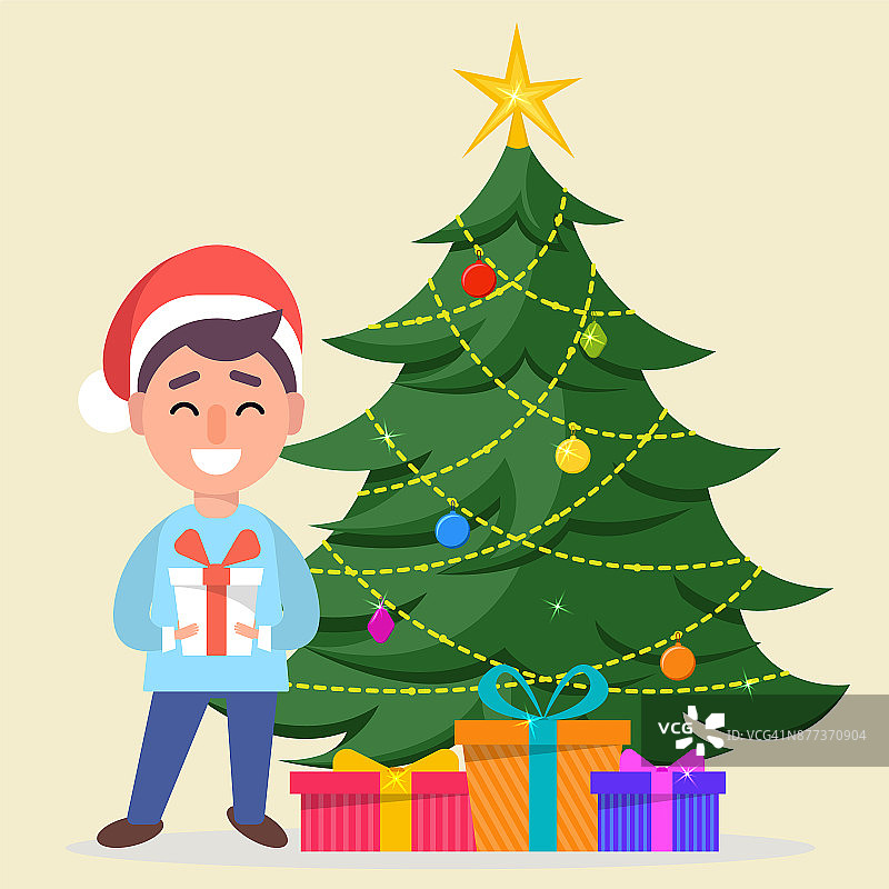 男孩戴着圣诞老人帽，站在装饰好的圣诞树旁，圣诞树下放着礼物盒图片素材