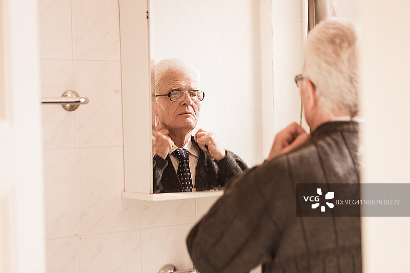 老年人在家里。老男人看着镜子里的自己，拿着衣服图片素材