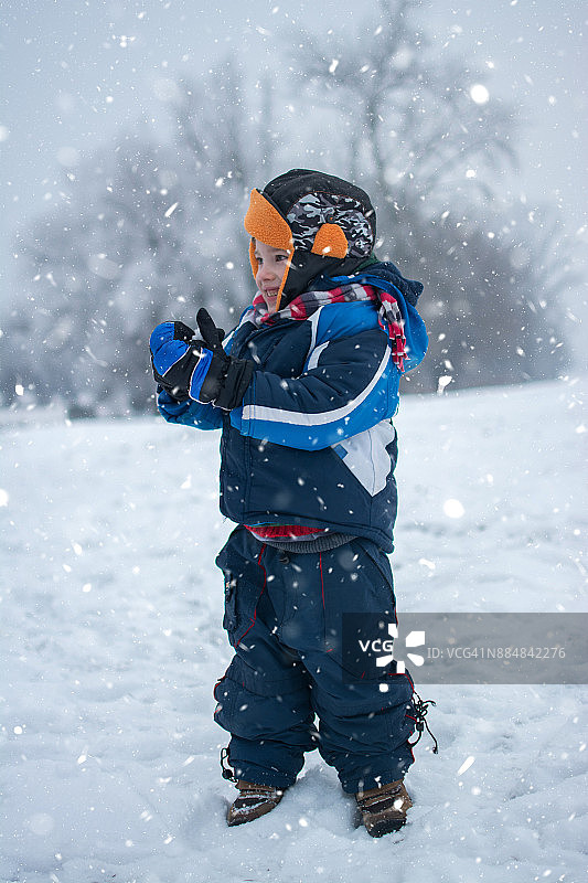 冬天公园里一个小男孩站在雪地上的全身像。图片素材