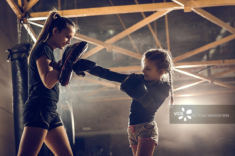 小女孩在健身俱乐部和教练练习拳击。图片素材
