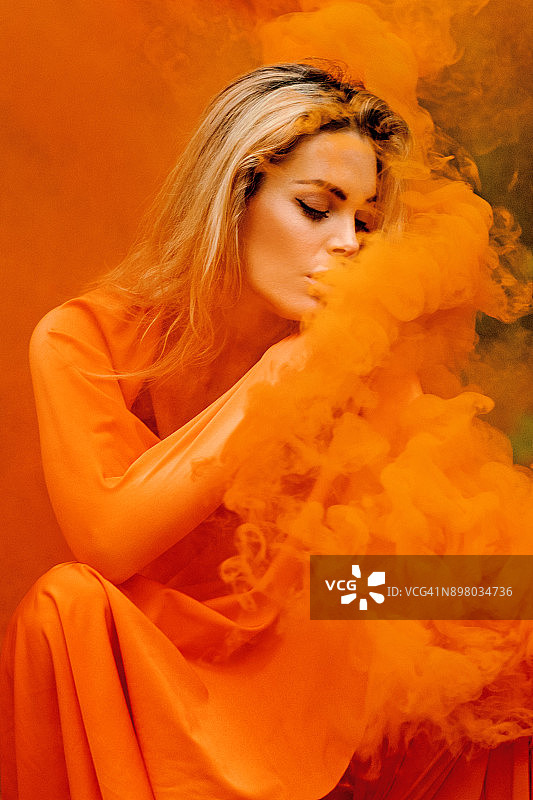 美丽年轻的金发女女人跳舞和摆姿势在室外乡村的橙色烟雾设置图片素材