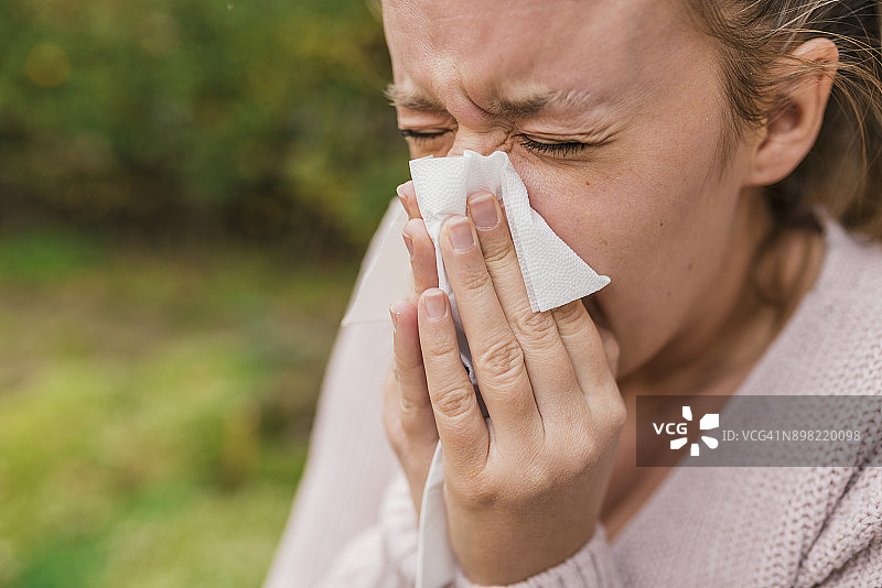 患有季节性流感的年轻女子用纸巾擤鼻子图片素材