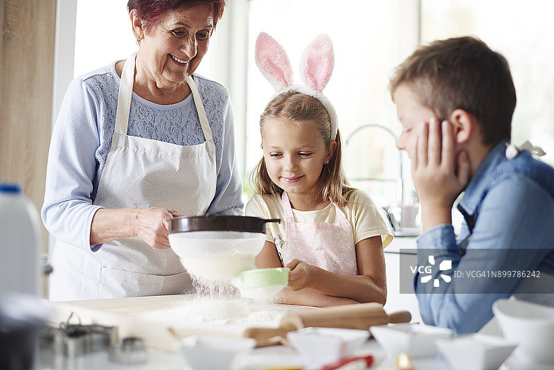 女孩和祖母在厨房柜台为复活节烘焙筛面粉图片素材