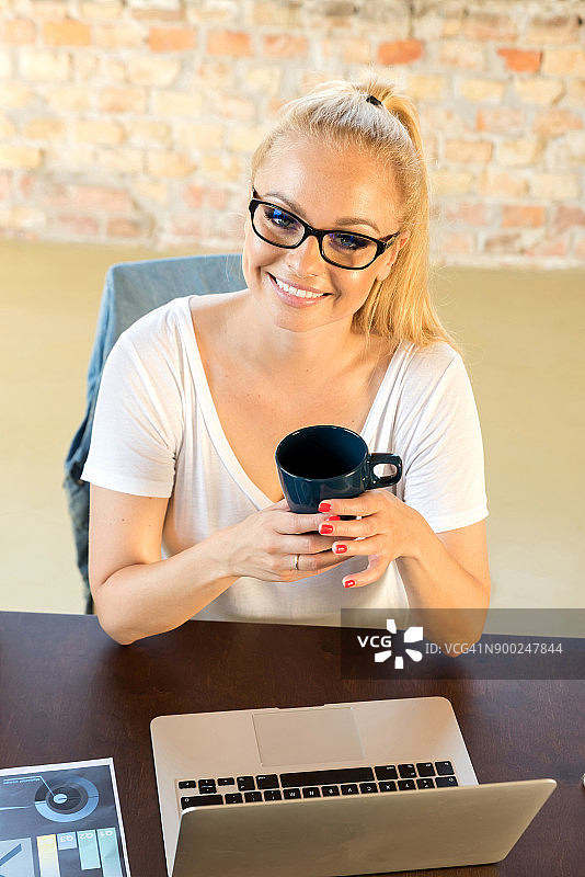 微笑的女商人坐在桌子上，咖啡杯图片素材