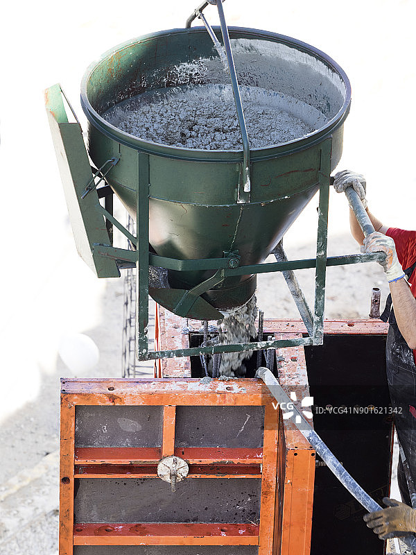 建筑工人在建筑工地工作，从起重机上卸下一桶混凝土。西班牙图片素材