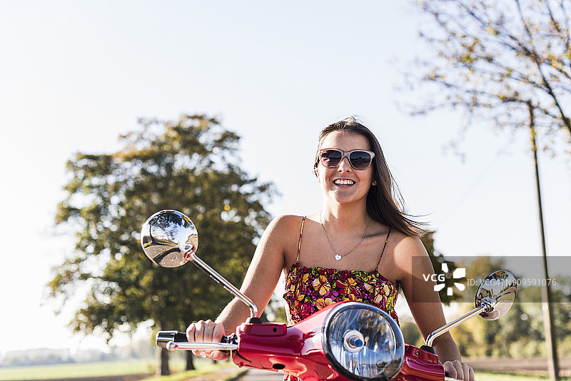 快乐的年轻女子骑摩托车在乡村公路上图片素材