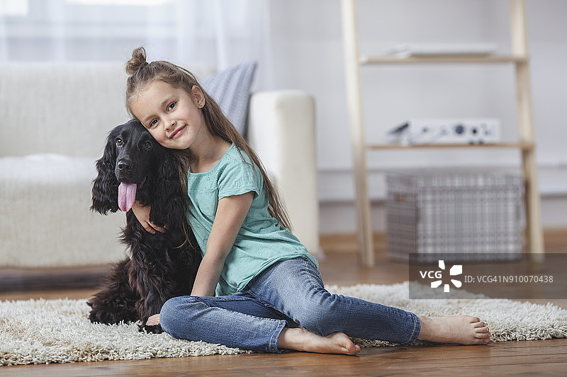 可爱的小女孩坐在地毯上拥抱小狗的肖像图片素材
