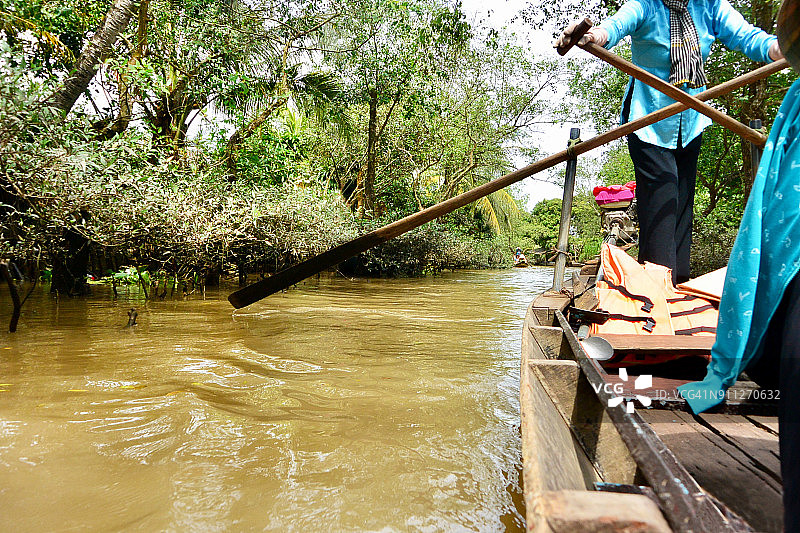 越南湄公河三角洲运河上的女子划着长桨图片素材