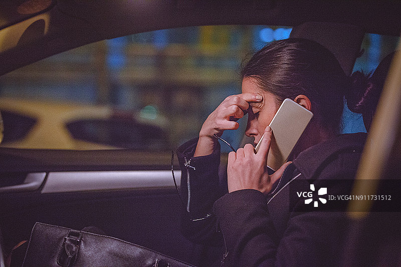 年轻女子晚上在汽车前座上使用智能手机图片素材