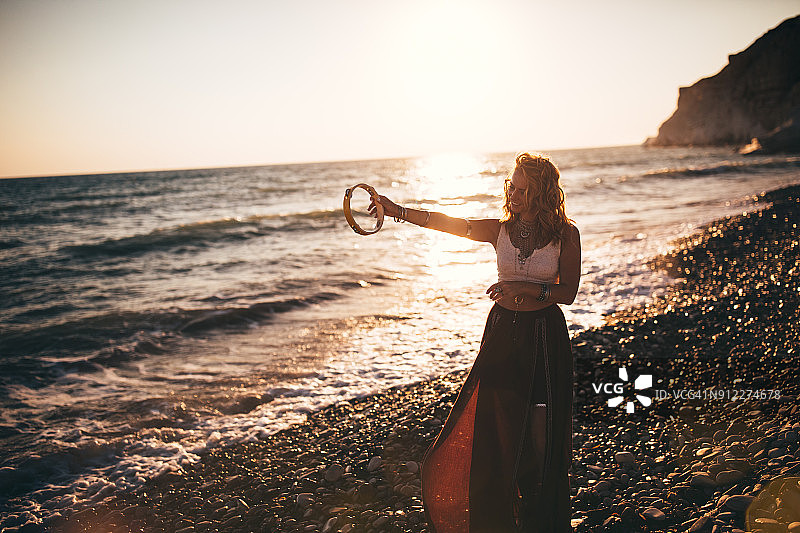 日落时分，波希米亚女子在海滩上打铃鼓图片素材