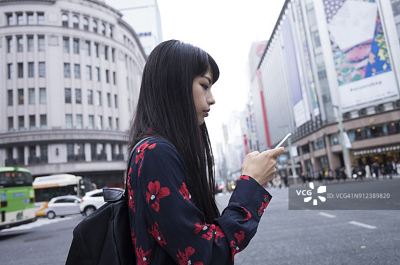 一个女人在市区看一个便携式屏幕。图片素材