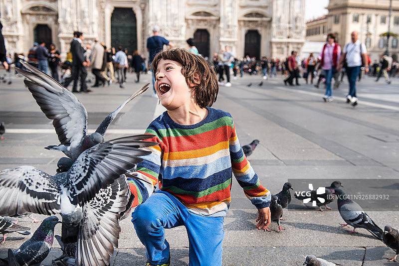 意大利伦巴第米兰，一个男孩在广场上喂鸽子时笑着图片素材