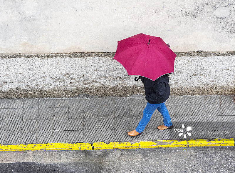 高角度的人与伞走在雨中与红色伞街道。瓦伦西亚,西班牙图片素材