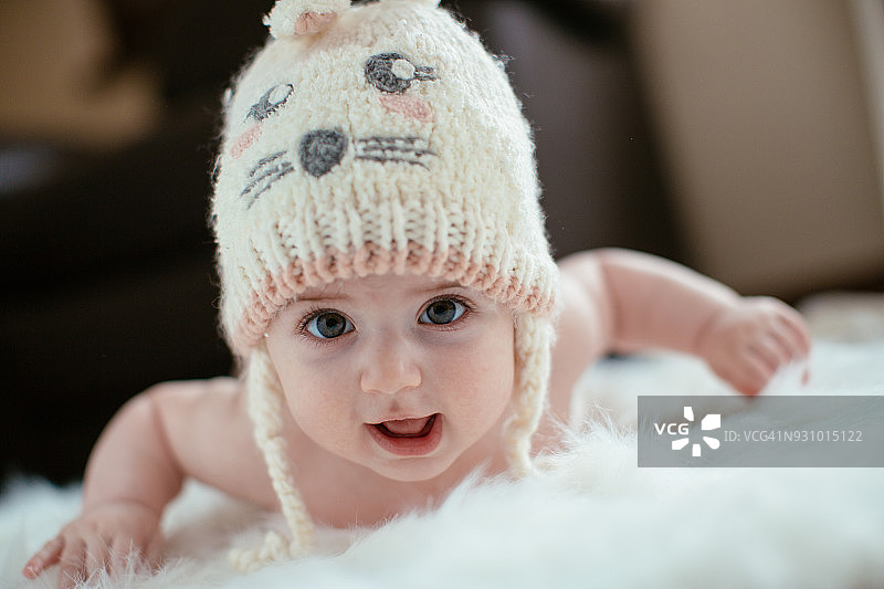 漂亮的婴儿戴着帽子爬在白色的地毯上图片素材