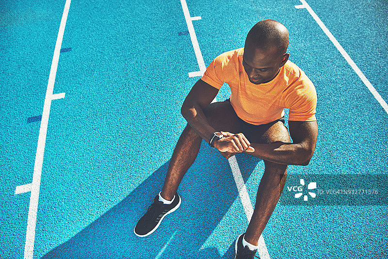 年轻的运动员坐在跑道上检查他的健身表图片素材