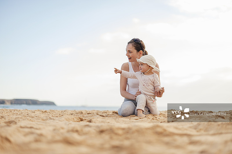 快乐的妈妈带着小女儿在海滩上图片素材