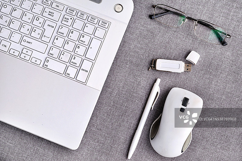 在灰色的办公桌上，戴着眼镜和笔记本电脑，近距离观察电脑键盘、笔和usb闪存。工作台工作台概念图片素材