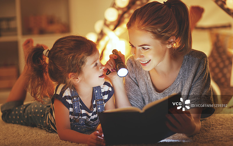 妈妈和孩子在睡觉前看一本书和一个手电筒图片素材