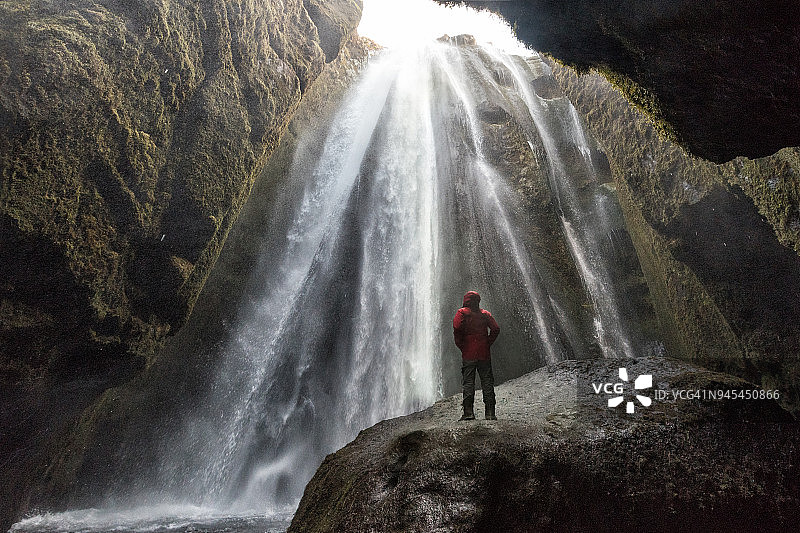 Gljufrabui或Gljufrafoss是冰岛南部美丽的瀑布之一。身穿红色皮大衣的旅行者站在岩石上，在狭窄的峡谷中有令人惊叹的瀑布。图片素材