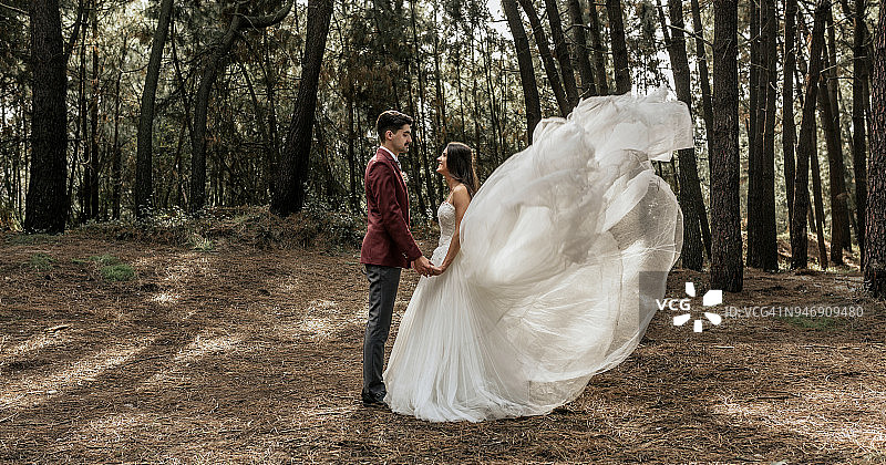 新娘穿着迎风婚纱，新郎手牵着手站在森林里图片素材