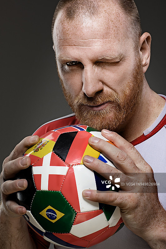 来自丹麦的蓄着胡须的红发成年男子足球运动员手持一个覆盖着国际国旗的足球图片素材